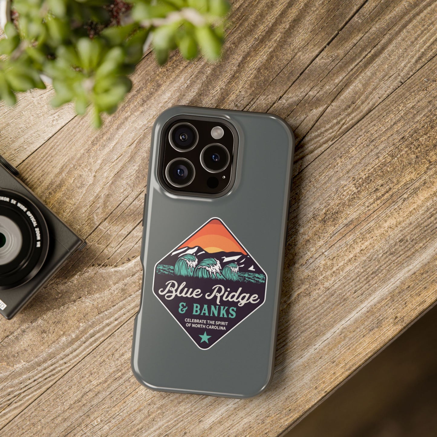 "Blue Ridge & Banks Magnetic Tough Case for iPhone 16 - Featuring a North Carolina-inspired design with nature elements, this durable phone case showcases a vibrant Blue Ridge Mountains motif. Perfect for outdoor enthusiasts and those who appreciate the beauty of nature, the case combines rugged protection with artistic flair, ensuring your device stays safe while reflecting your love for the scenic landscapes of the Blue Ridge region."