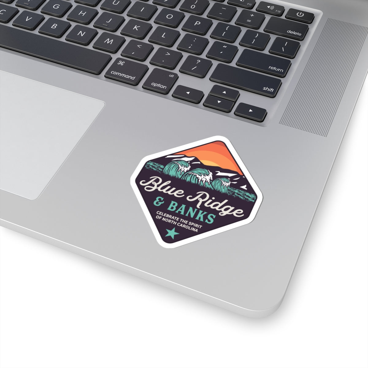 "Blue Ridge & Banks Logo Sticker – A vibrant 2x2 inch kiss-cut vinyl sticker featuring the iconic North Carolina brand logo. This durable and weather-resistant sticker showcases a nature-inspired design with elements reminiscent of the scenic Blue Ridge Mountains, perfect for outdoor enthusiasts and NC brand supporters. Ideal for personalizing laptops, water bottles, or any surface with a touch of North Carolina pride."