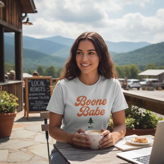 Woman wearing Boone Babe t-shirt at outdoor café with North Carolina mountains in background, lifestyle mockup