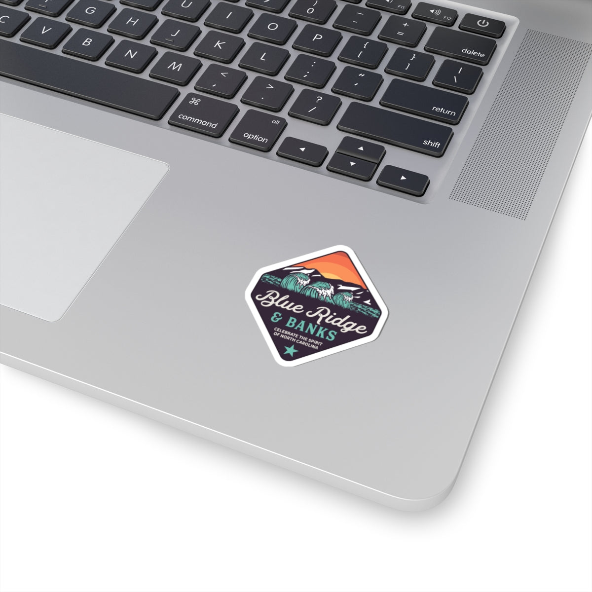 "Blue Ridge & Banks Logo Sticker – Kiss-Cut NC Brand Vinyl, 2\" × 2\" - Showcasing a sleek design, this North Carolina-inspired logo sticker features elements of nature, capturing the essence of the Blue Ridge Mountains. Perfect for outdoor enthusiasts and brand supporters, this high-quality vinyl sticker offers durability and a stylish touch to any surface."