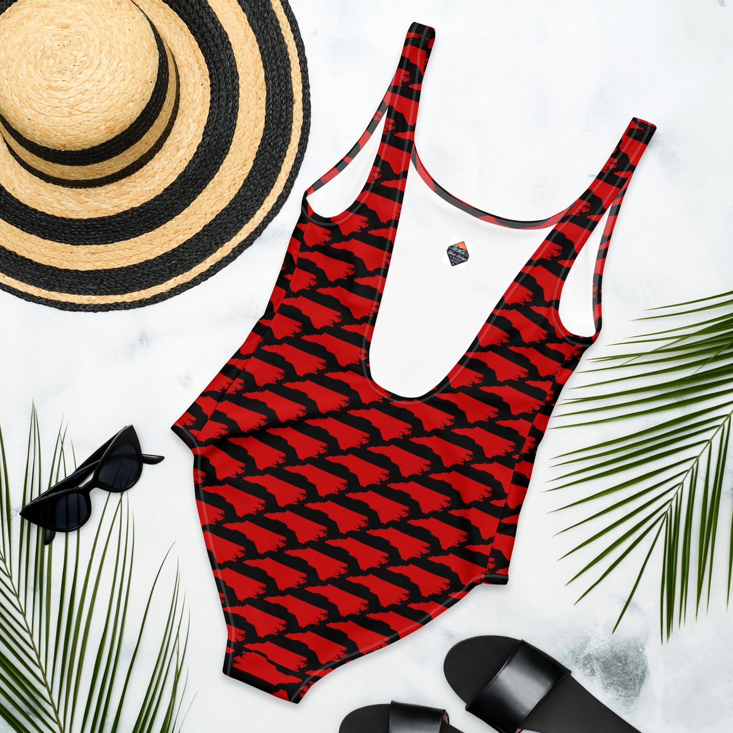 Flat lay of Carolina Inferno Swimsuit with beach accessories, bold red NC print on black