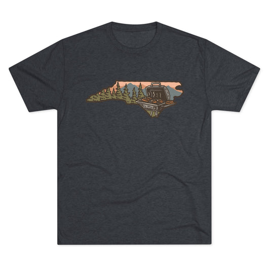 Navy T-shirt featuring a North Carolina state outline with a forest cabin, mountain backdrop, and backyard grill illustration.